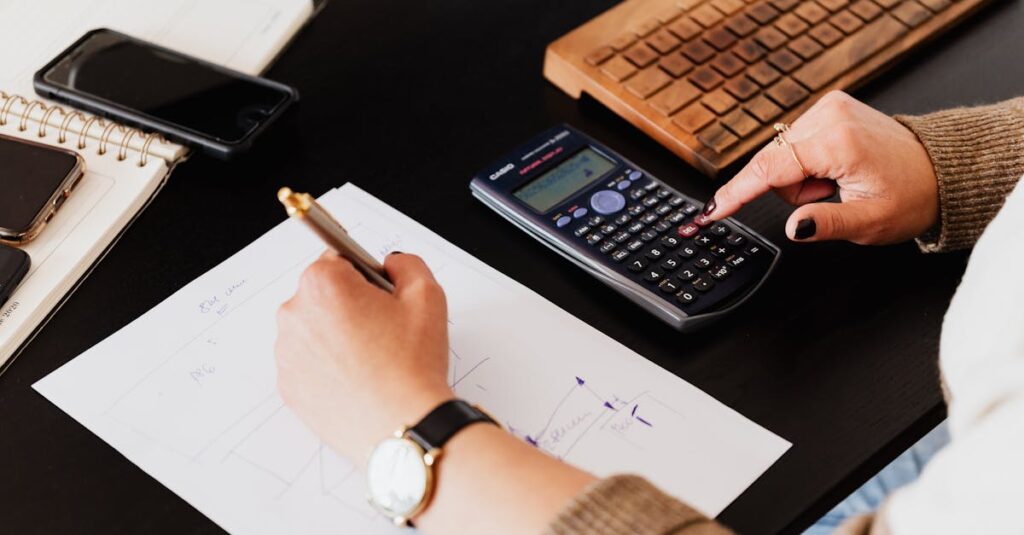 Close-up of hands working with a calculator and notebook on a desk, analyzing documents.
