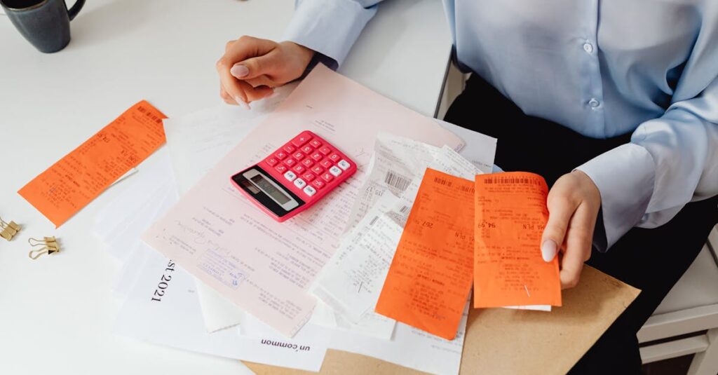 A woman reviews receipts and calculates expenses at a desk with a pink calculator.