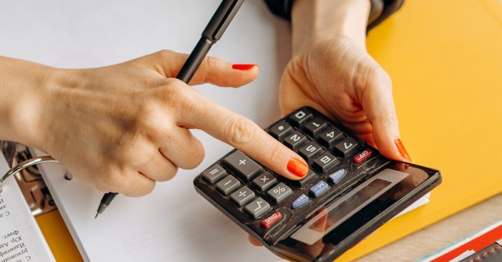 Close-up of a woman using a calculator at her wooden workspace with documents and notepads.